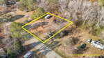 Aerial view of a rectangular plot of land outlined in yellow, with a camper parked near the center. The property is bordered by a road, trees, and neighboring lots. Text notes that property lines are estimated.
