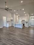 Open-concept kitchen and living area with white cabinets, pendant lights over an island, stainless steel appliances, and light gray walls. Wood-style flooring extends throughout the space. Ceiling fan and recessed lighting are visible.