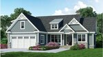 A modern single-story house with blue siding, white trim, a front porch, dormer windows, a two-car garage, and landscaped shrubs in front, set against a background of trees and blue sky.