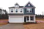 A two-story modern house with gray siding, white trim, and a blue accent section. There is a two-car garage, a covered front porch, and the yard appears to be unfinished with bare soil and minimal landscaping.