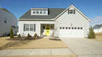A gray suburban house with white trim, a front porch, a yellow door, an attached two-car garage, and well-kept landscaping, set against a clear blue sky.