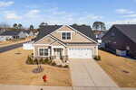 A single-story suburban house with beige siding, white trim, and a two-car garage sits on a large lot with a concrete driveway and minimal landscaping. A red fire hydrant is visible near the driveway.