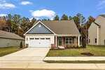 A single-story house with a two-car garage, gray and blue siding, and brick accents. It has a paved driveway, a small front porch, and a neatly landscaped lawn with young trees, set in a suburban neighborhood.