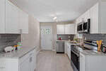 Modern kitchen with white cabinets, stainless steel appliances, gray subway tile backsplash, granite countertops, and light wood flooring. A door with a window is at the back, and small kitchen items are on the counters.