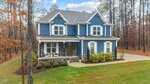 A two-story blue house with white trim, stone accents on the lower facade, a covered front porch, and a curved driveway, surrounded by trees and a well-maintained lawn.