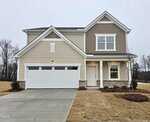 Two-story beige house with a double garage, white trim, and brown shingles on the upper level. The house has a small covered entryway, a concrete driveway, and a lawn with minimal landscaping.