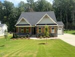A single-story house with a covered front porch, stone and wood siding, gable roof, a one-car garage on the right, a concrete driveway, and a well-maintained front lawn with small trees and shrubs.