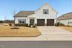 A single-story suburban house with white siding, brown double garage doors, a covered entryway, and a neatly maintained front lawn with minimal landscaping, situated on a clear day.