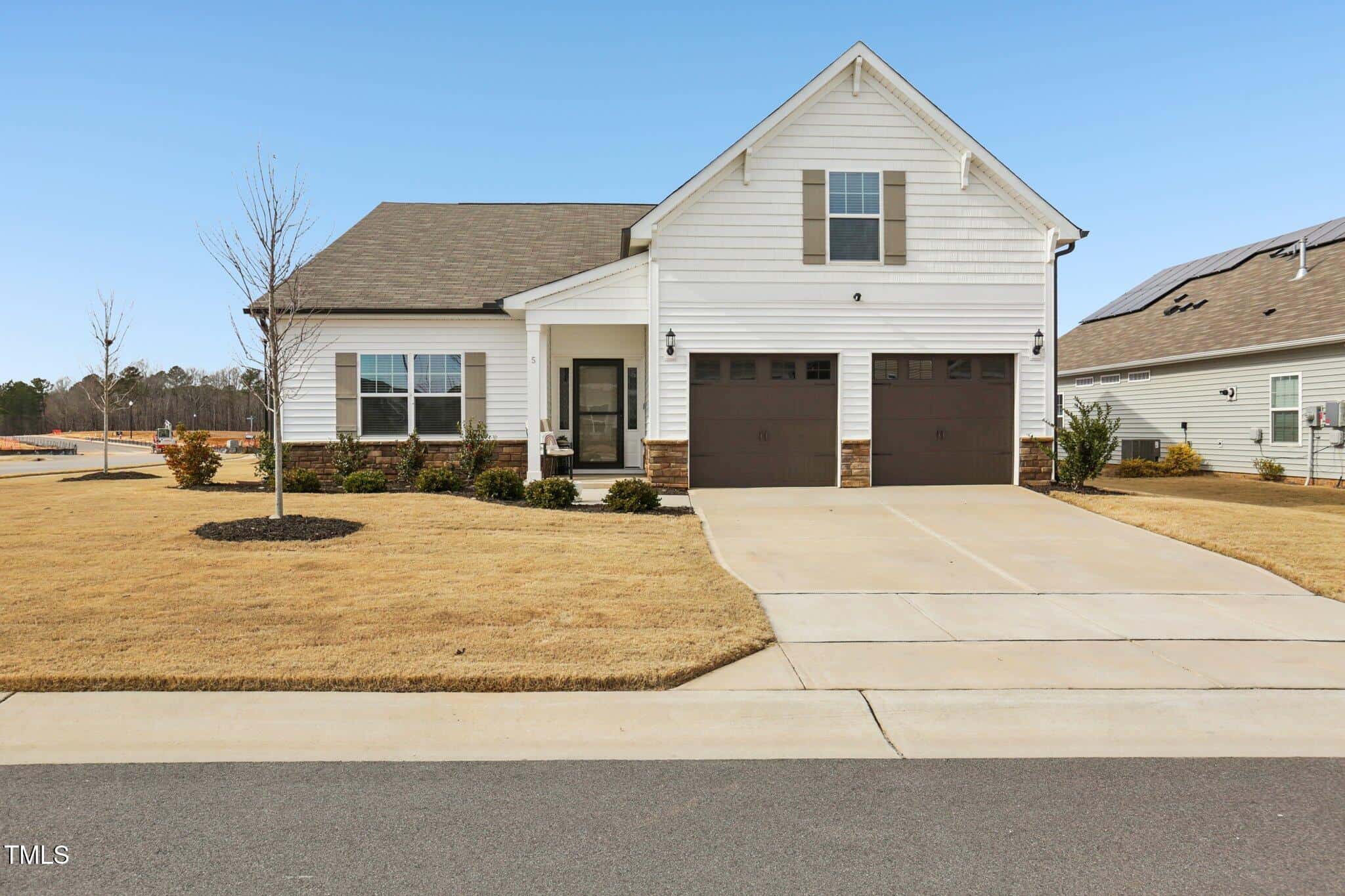 A single-story suburban house with white siding, brown double garage doors, a covered entryway, and a neatly maintained front lawn with minimal landscaping, situated on a clear day.