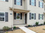 The exterior of a beige townhouse with white trim, black shutters, and a covered entryway. The house number "2025" is visible, and there is minimal landscaping with some grass and small shrubs.