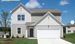 A two-story suburban house with light gray siding, white trim, and a white double garage door. The home has a small front yard with mulch, grass, and young shrubs under a blue sky.