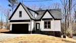 A modern, two-story house with white siding, black trim, a black roof, and a two-car garage. The home sits on a slightly sloped, dry lawn with trees and clear sky in the background.