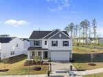 A two-story modern suburban house with white siding, gray accents, a front porch, double garage, and a well-maintained front yard. The home is situated in a residential neighborhood with trees and clear skies.