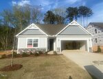 A single-story house with gray siding, white trim, and a covered front porch. A "SOLD" sign is visible in the front window. There is a driveway, minimal landscaping, and another house under construction nearby.