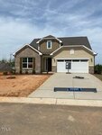 A newly built, two-story suburban house with a sold sign near the front window. The home has a two-car garage, brick and siding exterior, unfinished landscaping, and a concrete driveway under a partly cloudy sky.