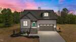 A modern gray house with stone accents, a teal front door, and a two-car garage sits on a spacious lot with a landscaped front yard, against a vibrant sunset sky with scattered trees in the background.