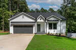 A modern white house with black accents, a two-car garage, and a front porch, set on a lush green lawn with trees in the background under a partly cloudy sky.