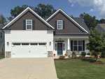 A modern suburban house with white siding, dark brown gables, stone accents, and a double garage. There is a covered front porch with a red wreath on the door, decorative plants, and a neatly landscaped yard.
