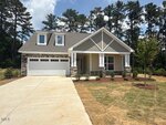 Single-story suburban house with gray siding, white trim, and stone accents, featuring a covered front porch, two dormer windows, a double garage, and a newly landscaped yard with trees and a driveway.