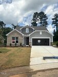 A single-story house with brick and gray siding, a two-car garage, and a "SOLD" sign in the front yard. The lawn is partly brown, with small bushes by the entrance, under a blue sky with clouds.