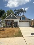 Single-story house with brick and siding exterior, white trim, two-car garage, covered entryway, small front yard with young plants, and a concrete driveway under a partly cloudy sky.