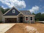 A newly constructed gray house with a stone entryway and a two-car garage sits on a dirt lot. A "SOLD" sign is visible in the front window, and the sky above is partly cloudy.