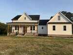 A two-story modern farmhouse with white board and batten siding, a black roof, covered front porch with wooden columns, and brick steps, set on a grassy yard during daylight.