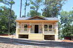 A small house under construction with exposed wood framing, partially covered in house wrap. A "Private Property" sign is posted on the front porch. Trees surround the area, and the sky is clear and blue.