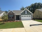 A single-story suburban house with a brick and gray exterior, a white garage door, and a manicured lawn. A "SOLD" sign is visible in one front window. The driveway is wide and clean.