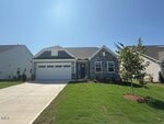 A single-story house with a stone and siding exterior, two-car garage, and a "sold" sign in front. The house has a well-kept lawn, driveway, and a newly planted tree, under a clear blue sky.