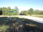 A rural roadside scene shows a street sign at the intersection of Dement and Aycock, with trees, grass, a pumpkin at the base of the sign, and a two-lane road stretching into the distance.