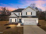 Two-story white house with black shutters, a double garage, a blue front door, and exterior lights on located at 690 Husketh Road in Youngsville. The lawn appears freshly landscaped, with leafless trees and a colorful sunset sky in the background.