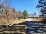 A paved road curves to the right through a rural area near 3004 US 401 Highway S, Louisburg, with leafless trees and patches of grass under a clear blue sky. The scene is quiet, with no vehicles or people visible.