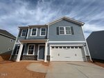 Two-story house with blue siding, white trim, a covered front porch, stone accents, and a double garage located at 69 Plantation Drive in Youngsville. The yard has red dirt with no grass yet. The sky is partly cloudy, and neighboring houses are visible on both sides.