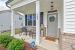 A front porch with two chairs and a small table sits outside a gray door with a "Welcome Home" mat and decorative sign. The house number 509 is on a column, and an ADT security sign is in the mulch bed.