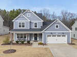 A two-story blue house with white trim at 125 Vast View Way, Youngsville, features a front porch with chairs, an attached two-car garage, and a neatly landscaped yard with small trees and shrubs in a tree-lined suburban neighborhood.