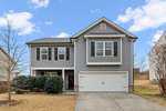 Two-story gray house with white trim, black shutters, and a double garage at 130 Ambergate Drive in Youngsville. The front yard features a driveway, some bushes, a bare tree, and a small lawn under a blue sky with a few clouds.
