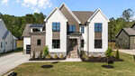 Modern two-story house at 125 Cherry Bark Drive in Youngsville, featuring white and brown siding, large windows, stone accents, and a manicured lawn. A stone porch leads to the entrance, with a driveway and garage on the left.