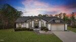 Charming single-story house at 73 Whippoorwill Lane with white exterior, black trim, arched windows, and a double front door; attached two-car garage on the right, surrounded by lawn, bushes, and trees beneath a sunset sky.