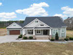 A modern single-story house at 540 Pine Ridge Road with light gray siding, dark gray roofing, and an attached two-car garage. The home features a front porch with columns, a large grassy yard, and a gravel driveway.