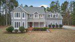 Two-story gray house with white trim, multiple gabled roofs, large windows, and a covered front porch situated at 4098 Charlie Harris Road, Oxford. Neatly trimmed bushes line the front of the home, which is surrounded by trees and features a stone path leading to the entrance.