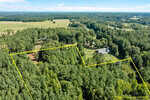Aerial view of a wooded rural property with estimated boundary lines marked in yellow, surrounded by dense trees, open fields, and a few houses visible in the clearing.