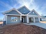 A newly constructed two-story house with gray siding, white trim, a covered front porch, a double garage, and unfinished landscaping under a blue sky.