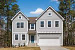 A two-story, light gray house with white trim, multiple windows, a blue front door, and a double garage, set against a backdrop of tall trees under a blue sky.