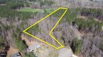 Aerial view of a wooded lot outlined in yellow, located at the end of a cul-de-sac. The surrounding area includes trees, a nearby house, and what appears to be a grassy field in the background.