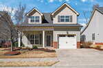 A two-story suburban house with beige siding, brick accents, and a single-car garage. There is a small front porch, a leafless tree in the yard, and a concrete driveway and sidewalk in front.