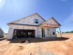 A partially constructed house with exposed framing and exterior sheathing, two front windows, an open garage, and a covered entryway sits on a dirt lot under a clear blue sky.