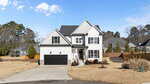 A two-story modern suburban house with white siding, black trim, and a black double garage. The house sits on a large, dry lawn with minimal landscaping and is surrounded by similar homes and trees.
