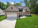 Charming single-story home at 116 Blackfoot Drive, Louisburg, featuring a stone and siding exterior, attached two-car garage, inviting front porch with white railings, and a manicured green lawn bordered by tall trees.