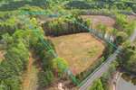 Aerial view of a rectangular, partially wooded plot of land at 6134 Bob Daniel Road, Oxford, bordered by a blue outline, showing grassy and forested areas, a road along one side, and surrounding trees.
